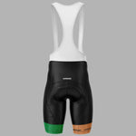 Rear view of a cycling bib short with a white upper section and black lower section, featuring green and brown textured accents at the bottom hems, on a solid gray background.